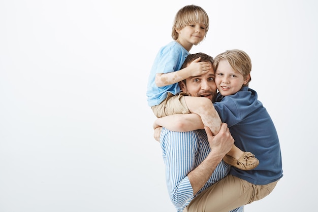 Cute positive family feeling great while playing together in park Portrait of happy goodlooking single father holding son with vitiligo on shoulders and older sibling on chest fooling around