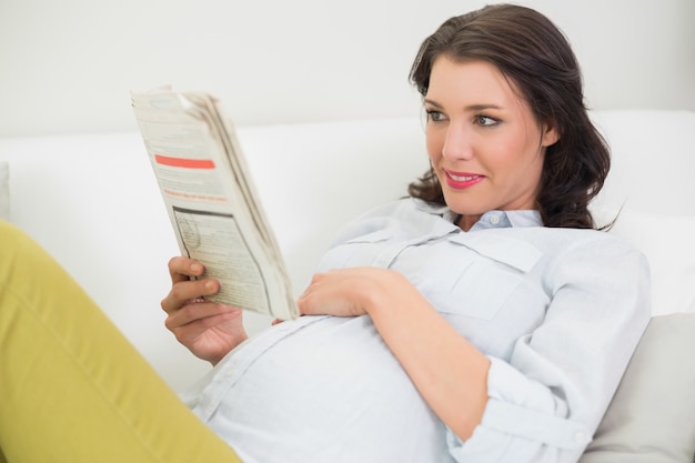 Foto donna dai capelli marrone incinta sveglia che legge un giornale
