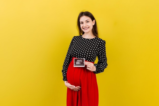かわいい妊娠中の女性が赤ちゃんの超音波検査写真でポーズをとって色付きの背景に近い