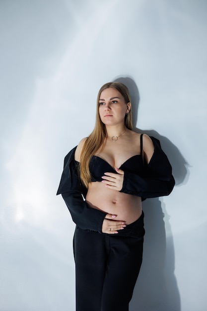 スタジオでかわいい妊婦 黒のスーツを着た妊婦 灰色の背景のスタジオ写真に美しい若い妊婦の幸せな妊娠中の女性の妊娠中の写真