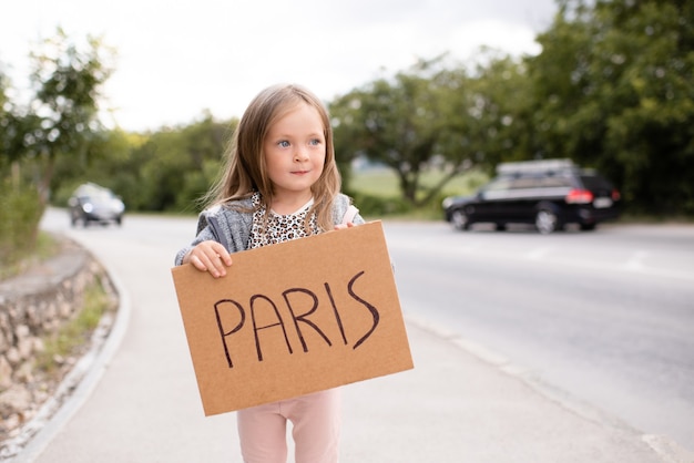 Cute pretty child girl travel with handwritten sign hitchhiking