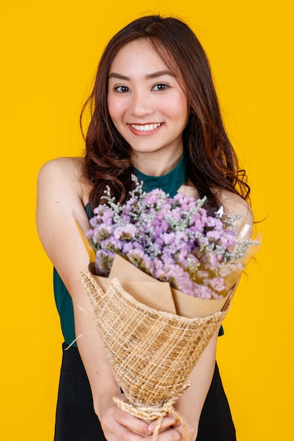 Симпатичные и довольно вьющиеся волосы Азиатская женская брюнетка, держащая букет цветов с веселой и счастливой, студийной съемкой, изолированной на ярко-желтом фоне.