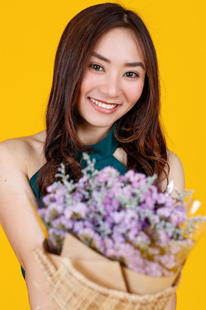 Симпатичные и довольно вьющиеся волосы Азиатская женская брюнетка, держащая букет цветов с веселой и счастливой, студийной съемкой, изолированной на ярко-желтом фоне.