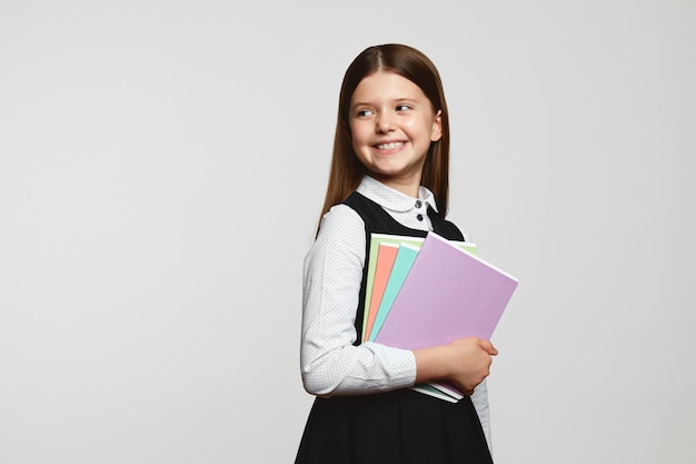 Foto la signora sveglia dell'allievo indossa l'uniforme scolastica che tiene i libri di testo in mano sorridendo e distogliendo lo sguardo