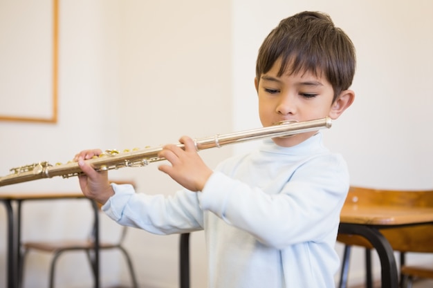 Cute pupil playing flute in classroom 