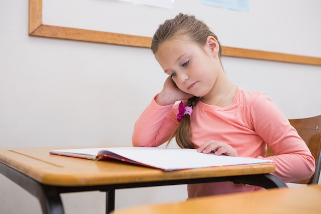 Cute pupil reading at her desk