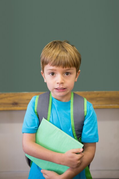 Photo cute pupil smiling at camera in classroom holding notepad