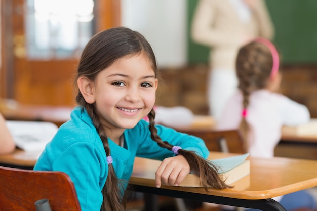 Allievo sveglio che sorride alla macchina fotografica al suo scrittorio in aula