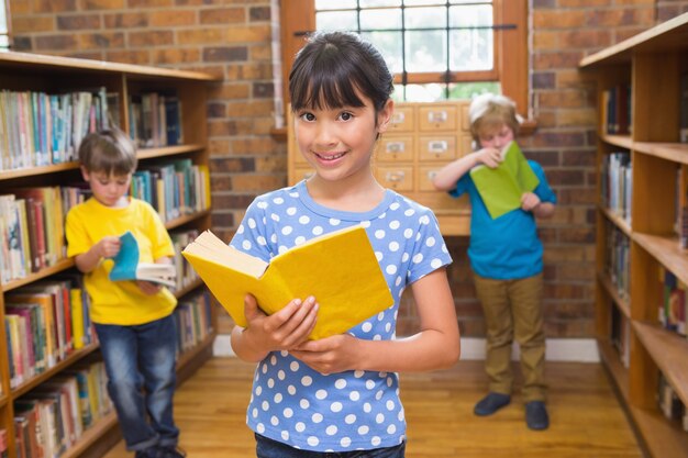 Cute pupil smiling at camera in library 