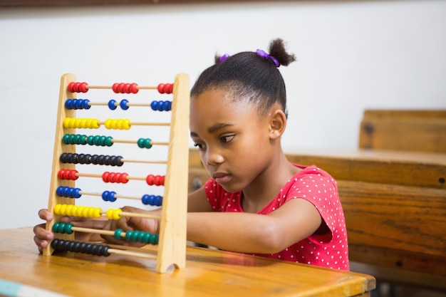 Photo cute pupil using abacus in classroom