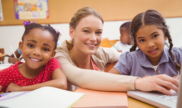 Cute pupil using computer with teacher