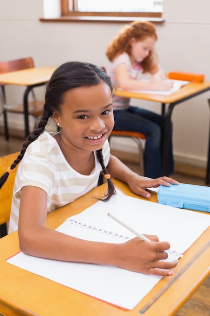 Cute pupils drawing at their desks one smiling at camera