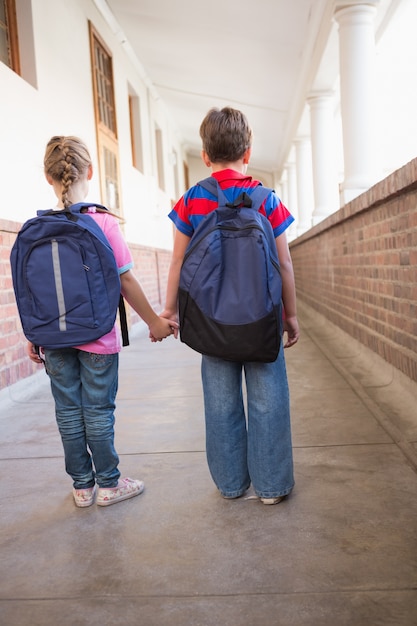 Cute pupils holding hands in corridor