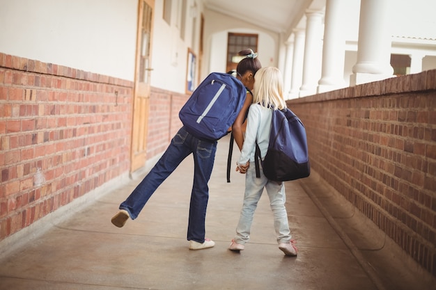 Cute pupils holding hands at corridor