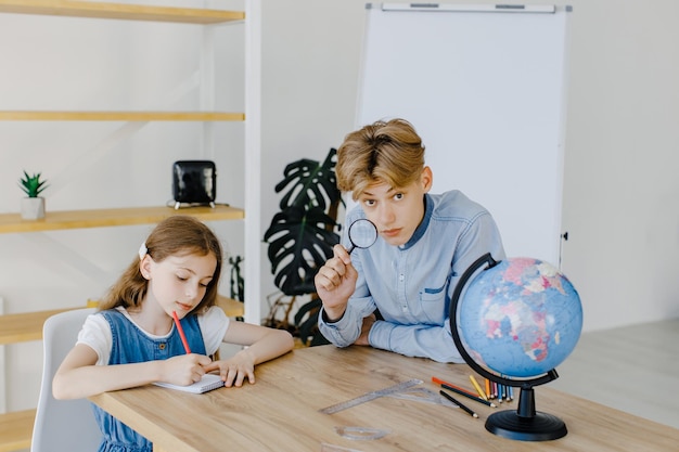 Cute pupils looking at globe in class at the school Boy holding magnifying glass and looking to the camera Conception of education