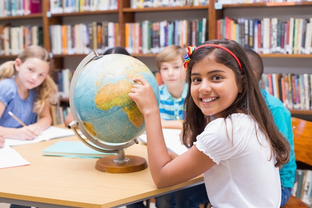 Cute pupils looking at globe in library