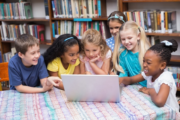 Cute pupils looking at laptop in library