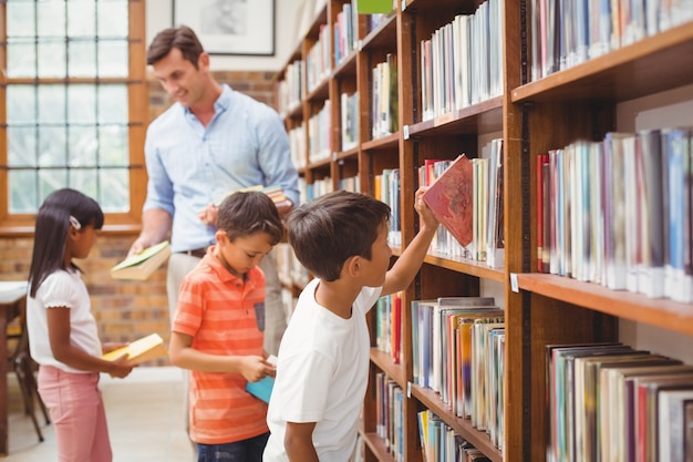 Cute pupils and teacher looking for books in library