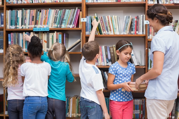 Cute pupils and teacher looking for books in library