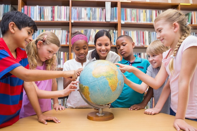 Cute pupils and teacher looking at globe in library 