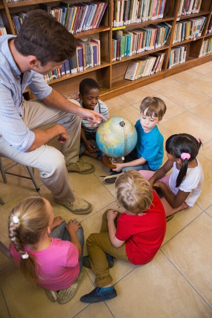 Cute pupils and teacher looking at globe in library