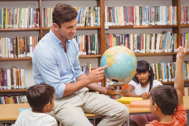 Cute pupils and teacher looking at globe in library