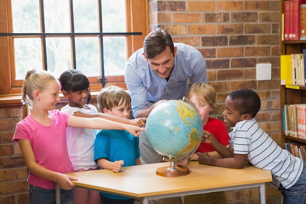 Cute pupils and teacher looking at globe in library