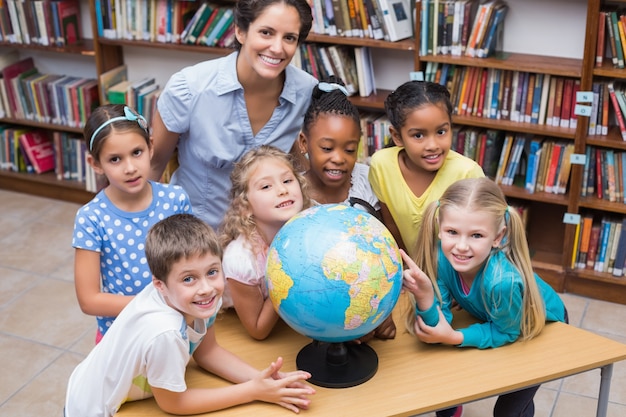 Cute pupils and teacher looking at globe in library