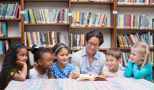 Cute pupils and teacher reading in library