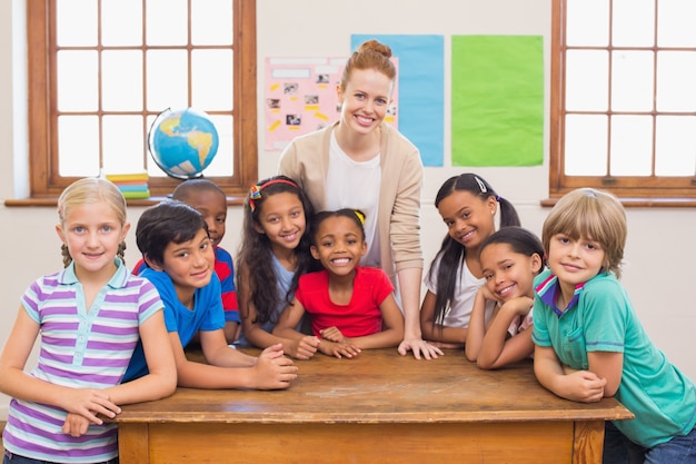 Cute pupils and teacher smiling at camera in classroom 