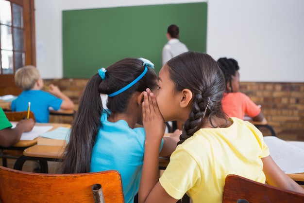 Cute pupils whispering in classroom