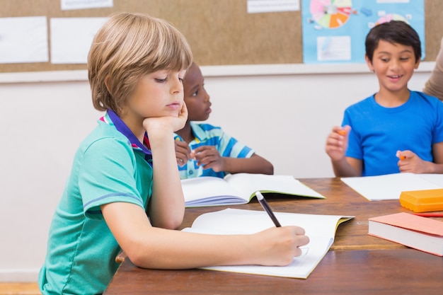 Cute pupils writing at desk in classroom 