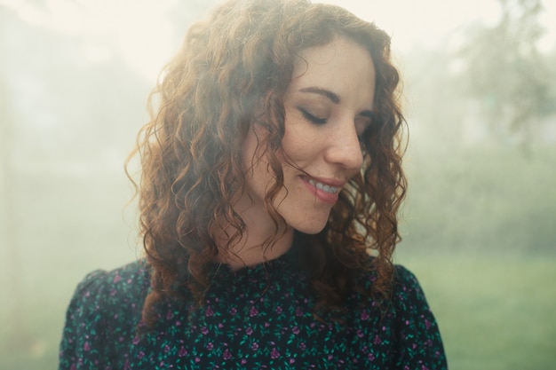 Cute red-haired curly girl rejoices under the water fogger in the city center