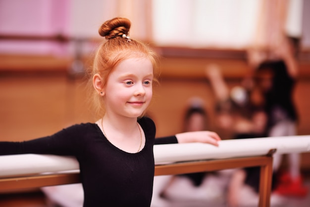 Photo cute red-haired girl ballerina stretching and doing the splits