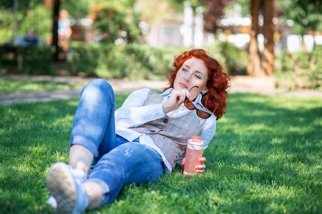 Cute red-haired girl lies in the park on the grass