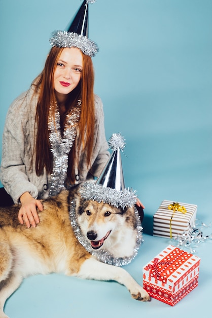 頭に帽子をかぶったかわいい赤毛の女の子が犬と一緒に床に座って、新年とクリスマスを祝います