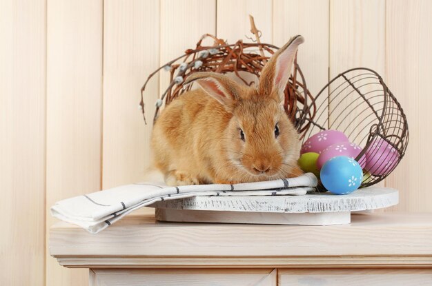 Cute red rabbit with Easter eggs on shelf on wooden wall background