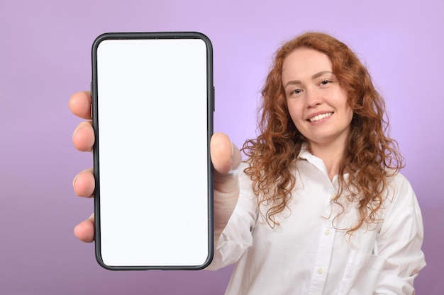 cute redhaired young woman holding phone with blank white screen