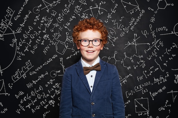 Foto piccola ragazzina dai capelli rossi in uniforme scolastica sullo sfondo della lavagna con formule scientifiche