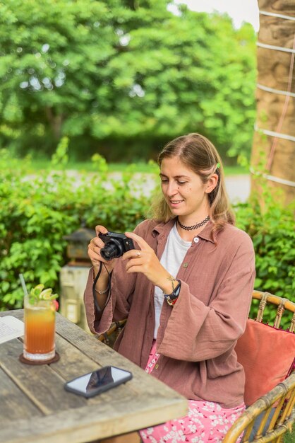 Cute russian woman taking a photo of ice tea in summer garden