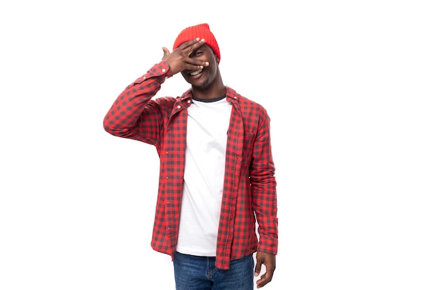 Cute s darkskinned american man dressed in a red shirt and hat covered his face with his hand on a