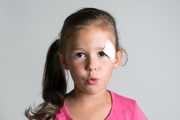 Cute sad disappointed dark haired little kid girl with injury\
scratch and patch plaster on face making lips in tube