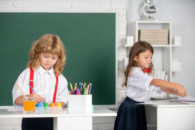 Bambini carini dei compagni di scuola che disegnano e dipingono a scuola ragazzo amichevole una ragazza alunni divertenti disegnano amici