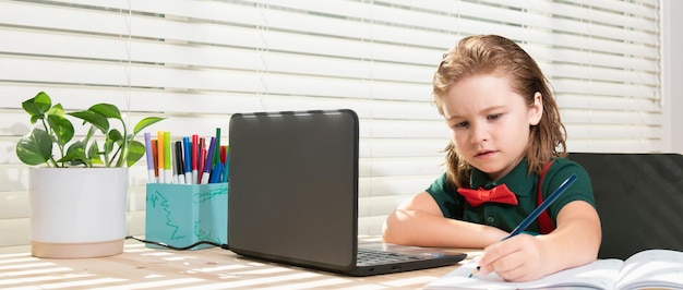 Cute schoolboy child does her homework with a tablet or laptop at home pupil writes the task in a no