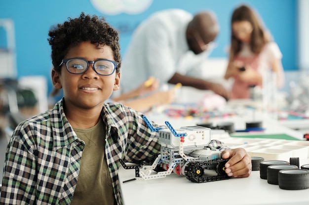 Cute schoolboy in eyeglasses and casual shirt holding self made robot