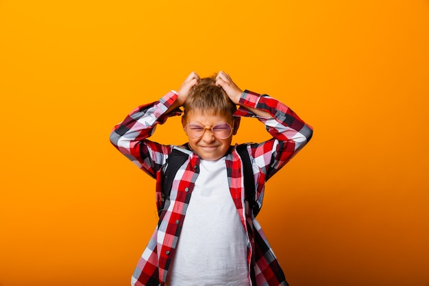 A cute schoolboy in a plaid shirt holds his head with his hands. isolation on a yellow background