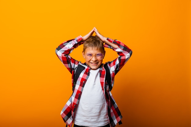 A cute schoolboy in a plaid shirt holds his head with his hands. isolation on a yellow background