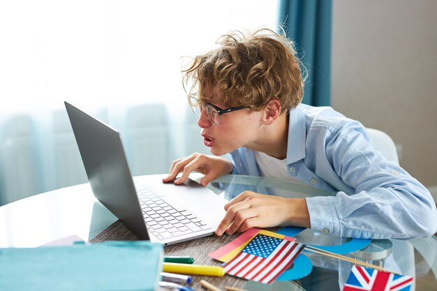 Cute schoolboy say hello at camera while having online lesson at home