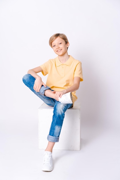 Cute schoolboy sitting on box wearing jeans and yellow tshirt isolated