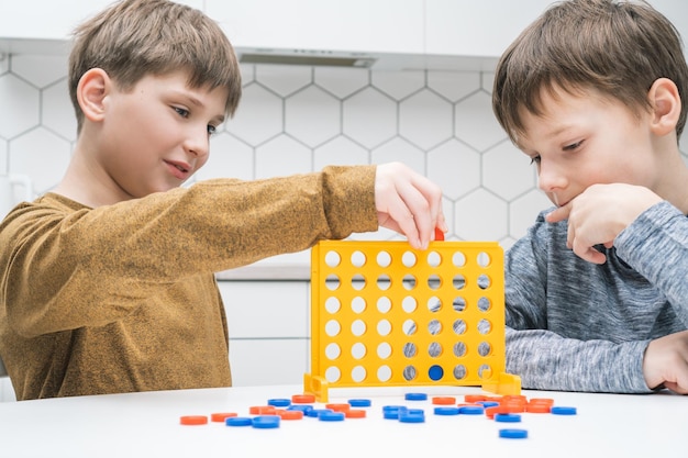 Cute schoolboys play toy constructor sitting at kitchen table Children collect plastic colored details of lego